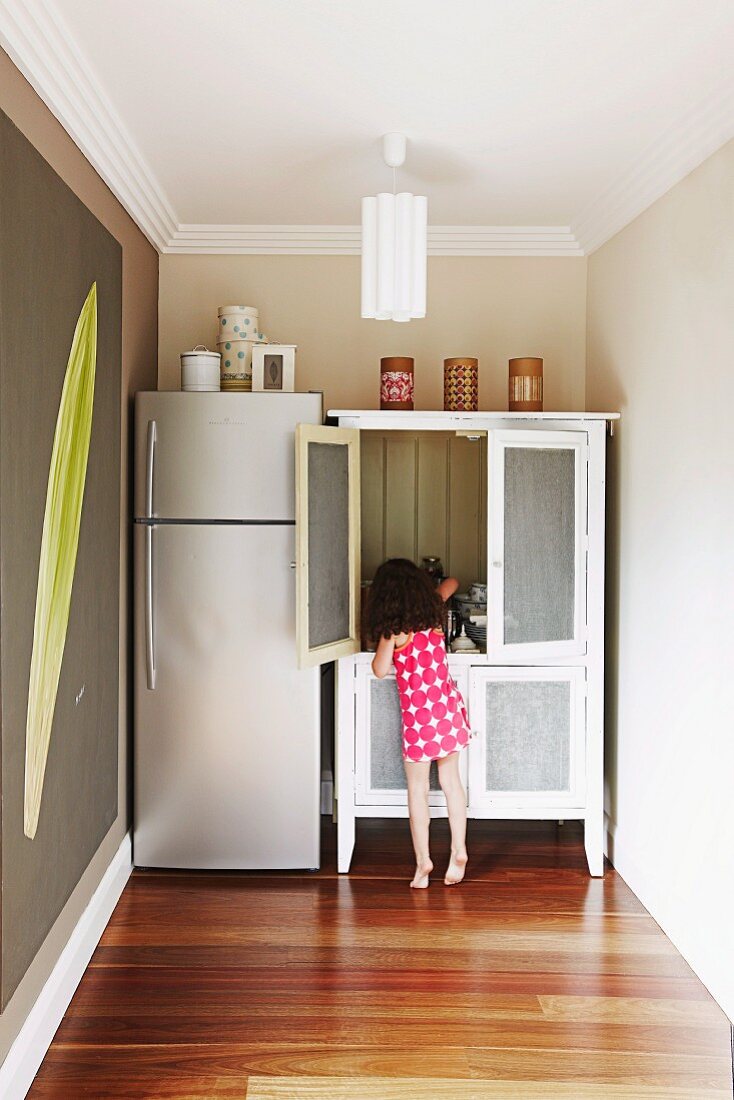 Little girl at cupboard next to fridge combination
