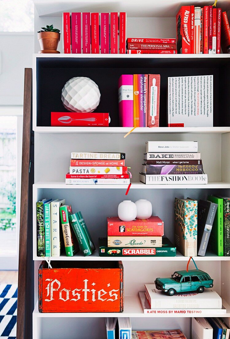 Books, vintage metal car and red-painted wooden box on and in white shelving modules on wall