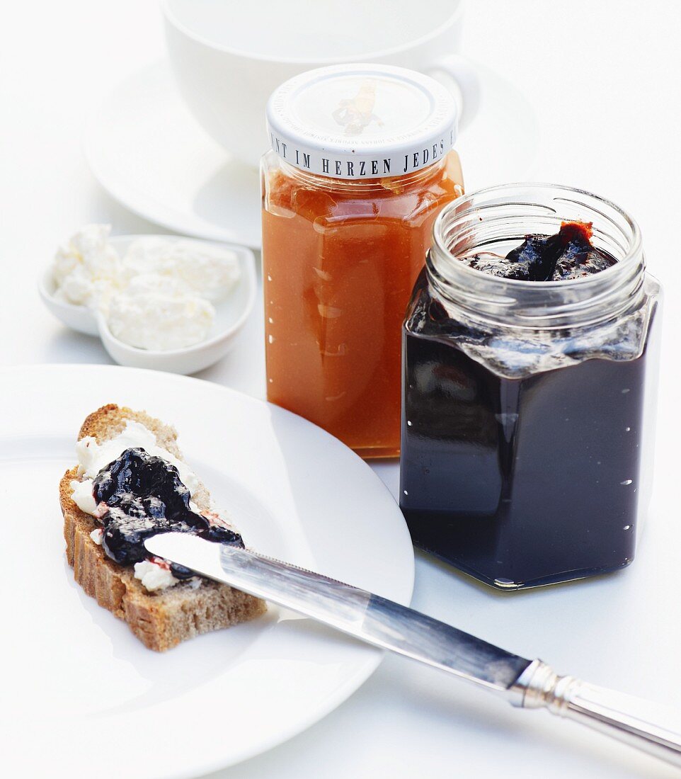 Bread topped with cream cheese and plum jam, with quince jelly in a jam jar