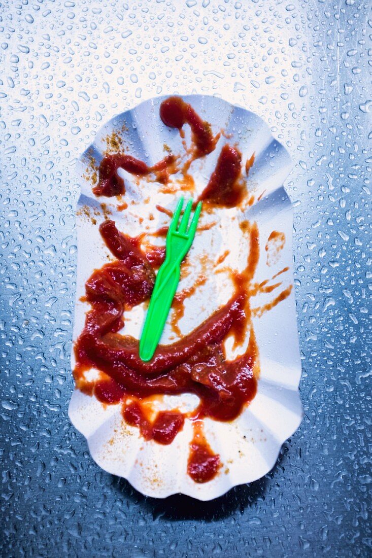 A dirty cardboard plate with the remains of currywurst with ketchup