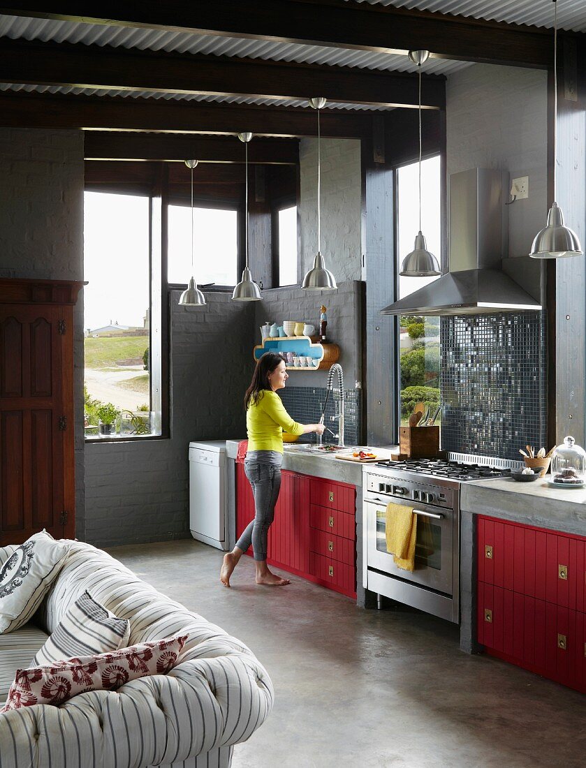 Offene Küche eines Architektenhauses mit roten Küchenfronten, Estrichboden und sichtbaren Deckenbalken
