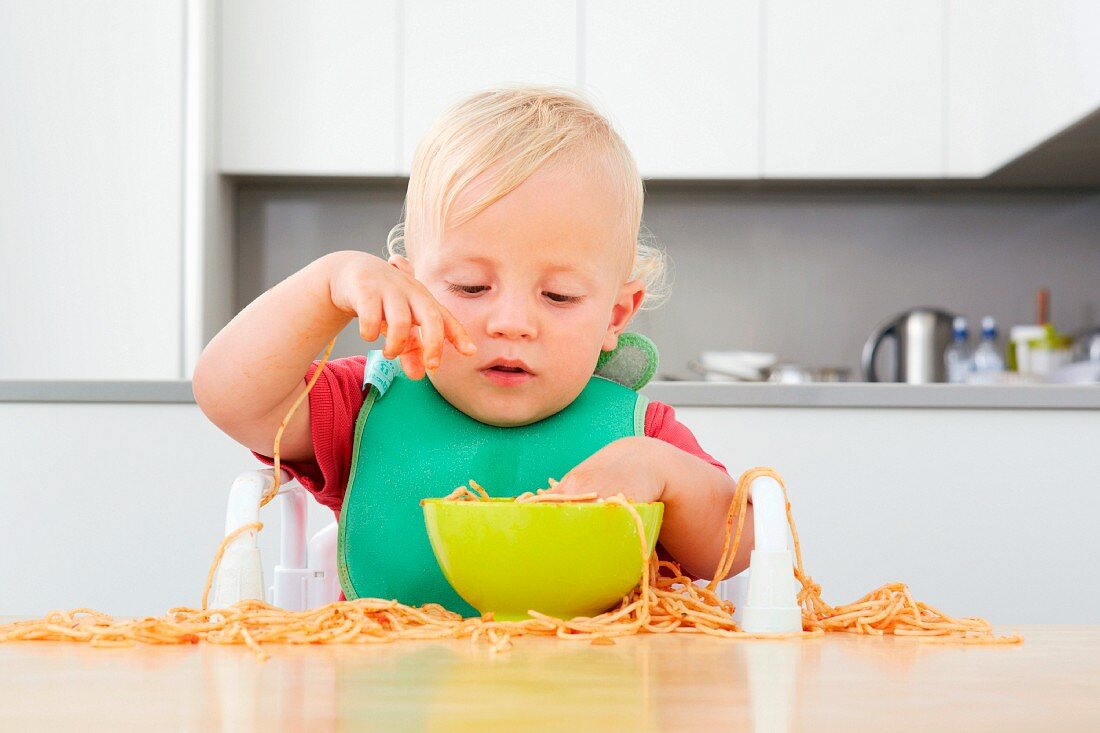 A small child playing with spaghetti
