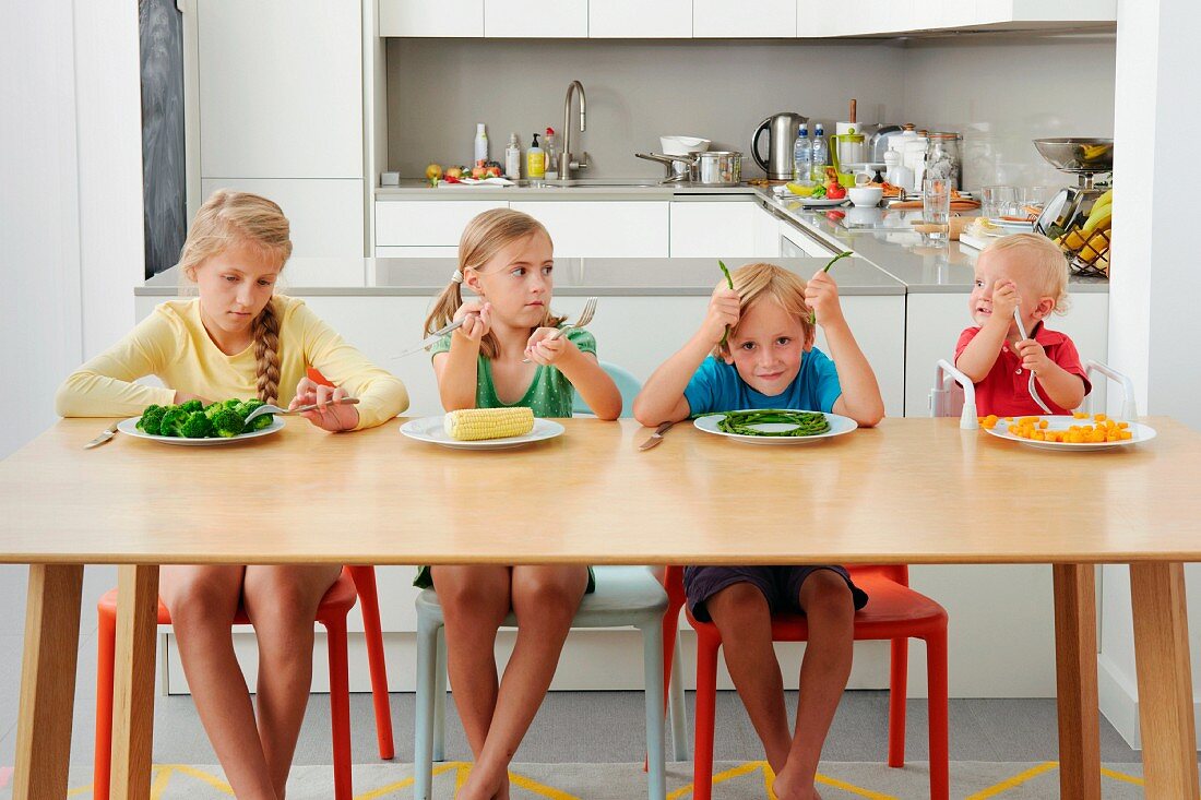 Vier Kinder sitzen gelangweilt vor Tellern mit Gemüse