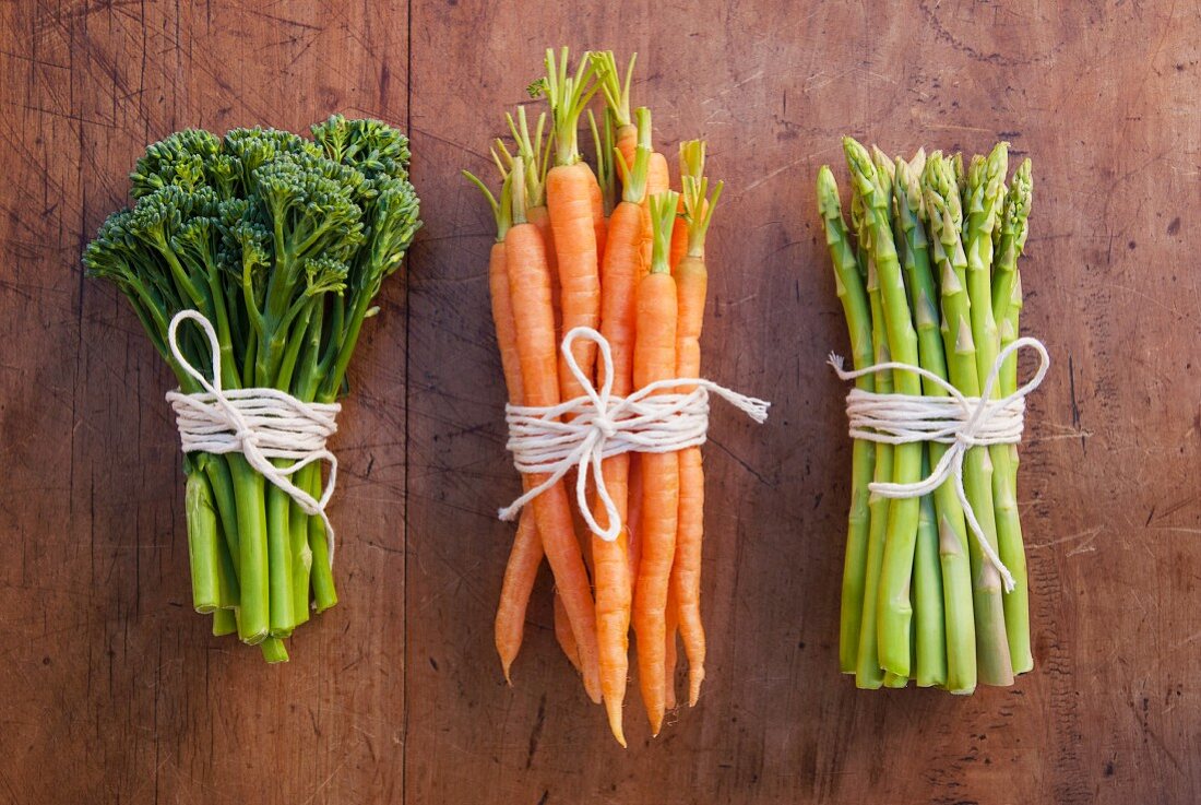 A still life featuring broccoli, carrots and green asparagus, tied in bundles