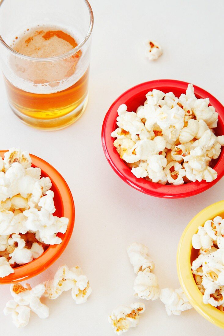 Popped Corn in Colorful Bowls with Glass of Beer. From Overhead