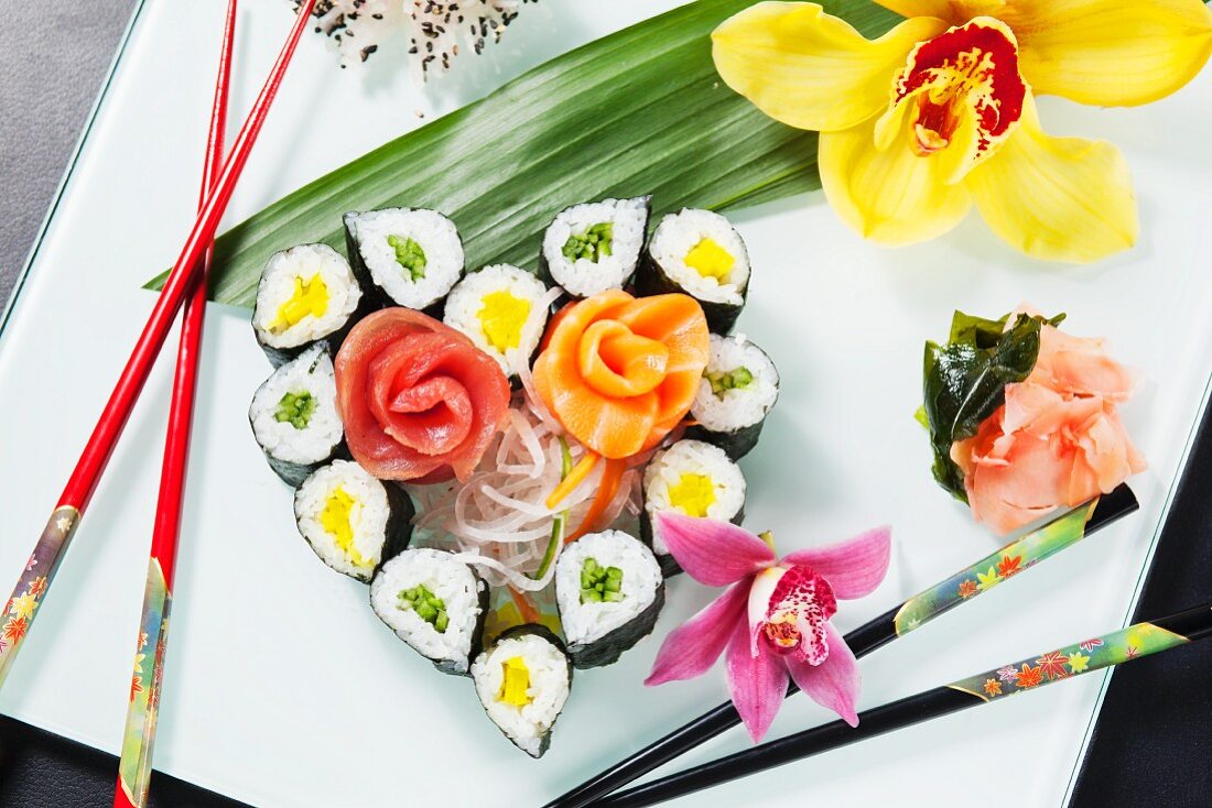 Assorted sushi in the shape of a heart with orchids and chopsticks