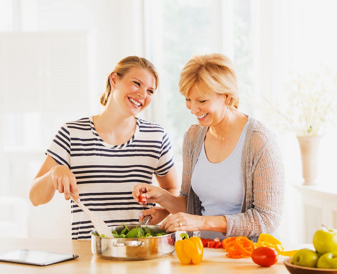 A mother and her adult daughter cooking together in the kitchen