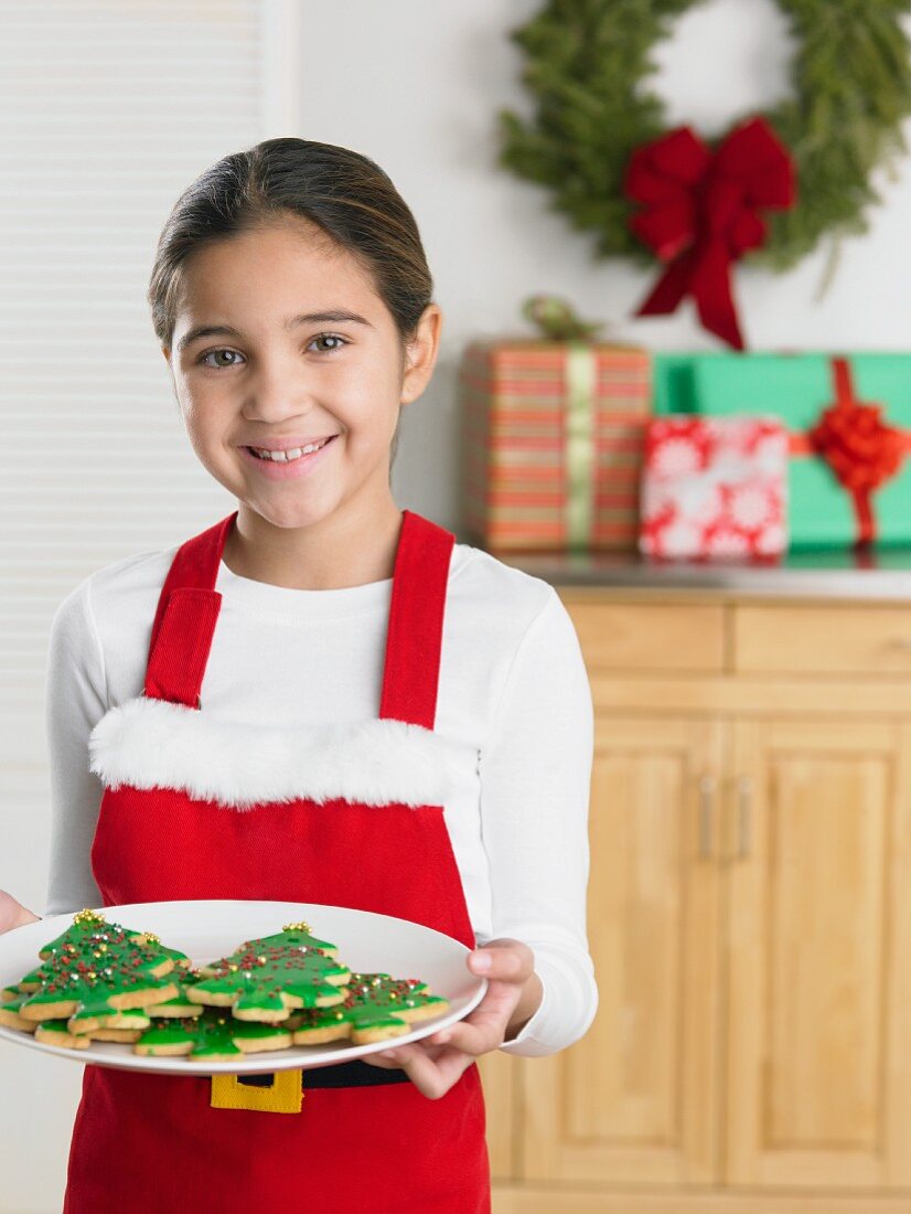 Young girl in a Santa apron holding a plate of Christmas cookies