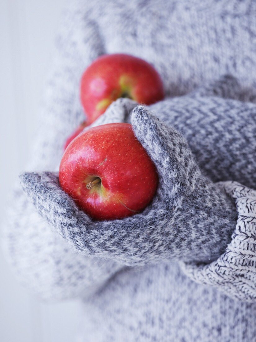 Kind mit Handschuhen & Wollpullover hält rote Äpfel