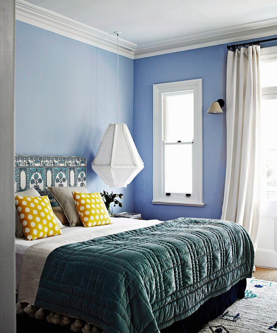 Double bed with quilt, yellow dotted pillows and ethnic pattern on bed head against pastel blue wall