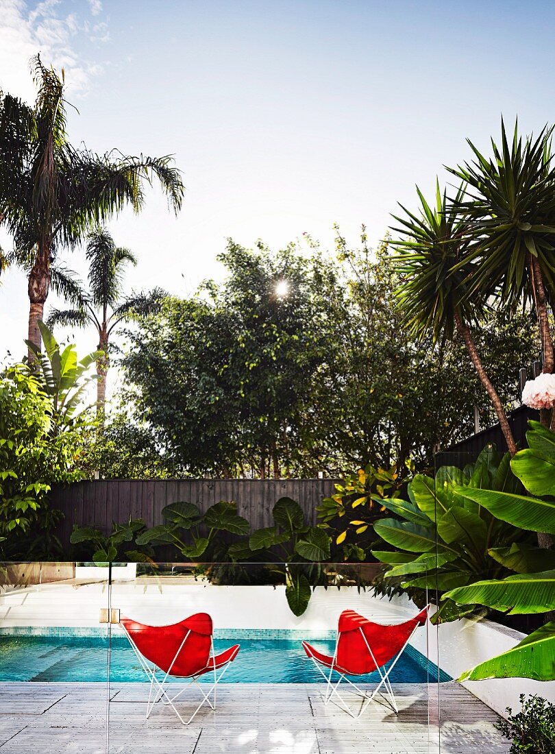 Pool with two red butterfly chairs behind glass balustrade