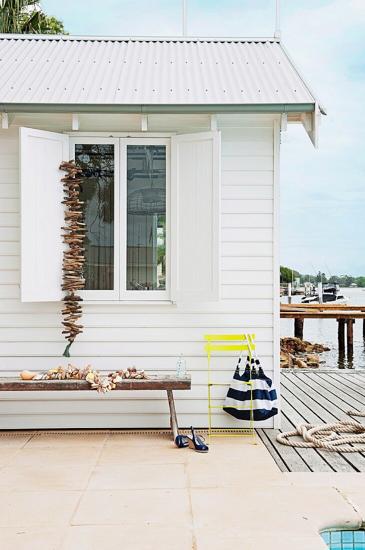 Weisses Strandhäuschen mit Muschel- und Schwemmholzdekoration; an der Hauswand eine lange Holzbank