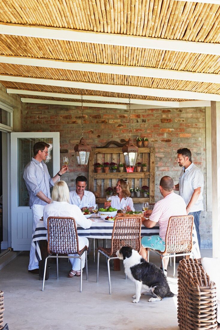 Gemütliche Essensrunde mit Freunden auf überdachter Terrasse mit Bambusabdeckung