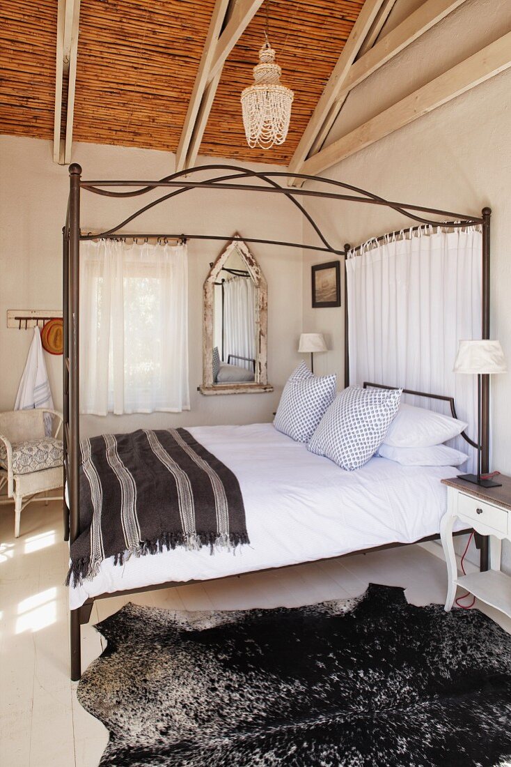 Four-poster bed with striped brown blanket and exposed roof structure with bamboo covering