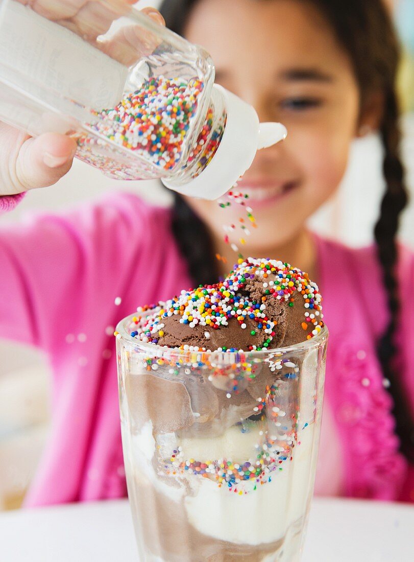 Mädchen schüttet Zuckerperlen über einen grossen Eisbecher