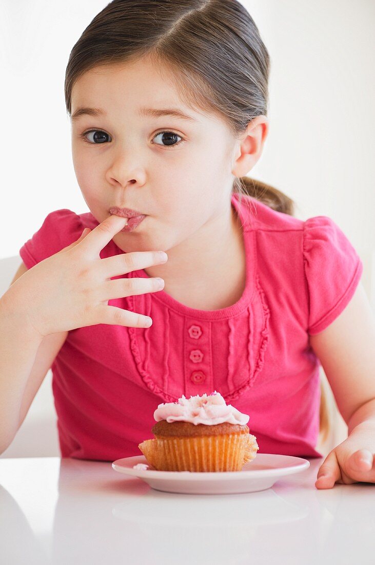 Mädchen mit Cupcake schleckt sich Zuckerguss von den Fingern