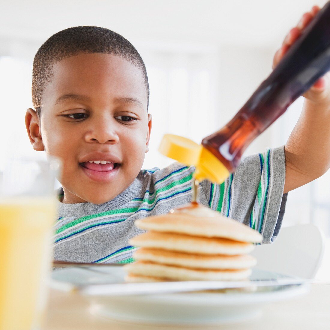 Arikanischer Junge giesst Ahornsirup auf Pancakes