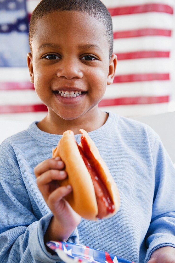 Lächelnder dunkelhäutiger Junge isst Hot Dog