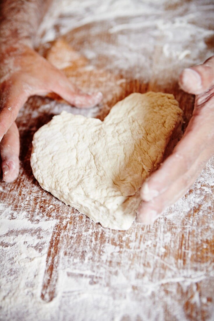 Hände formen herzförmiges Brot