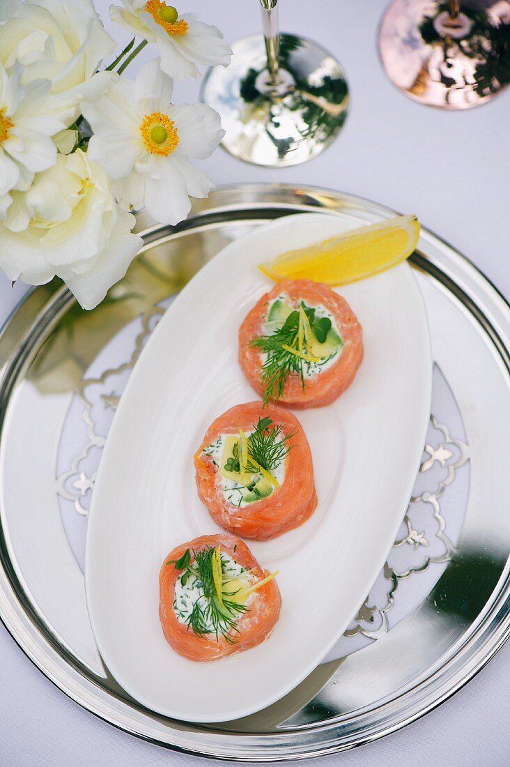 Smoked salmon rolls filled with goat's cream cheese and dill on a table laid for a party