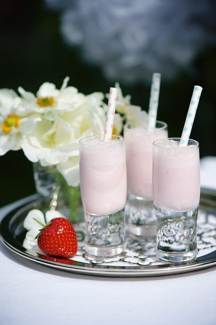 Erdbeer Milchshakes in kleinen Gläsern mit Trinkhalmen auf Silbertablett
