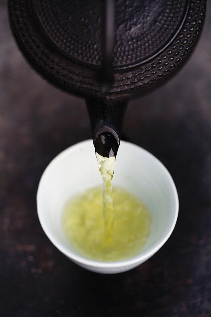 Close up of Japanese green tea being poured from teapot into cup