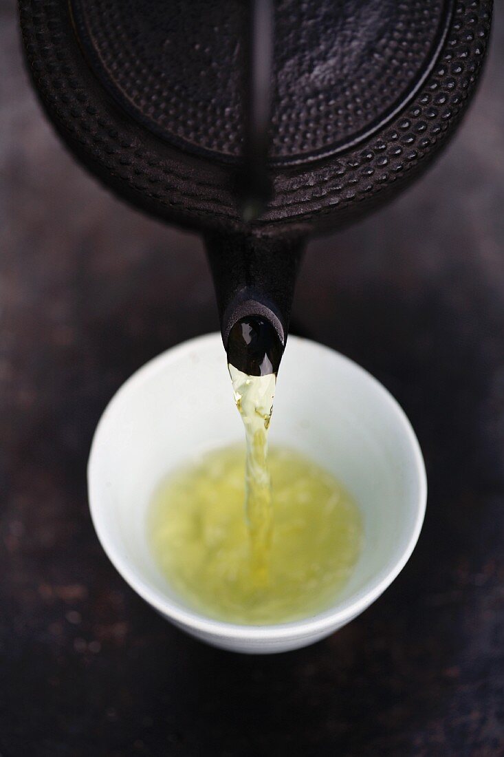 Grüner Tee wird aus Teekanne in Teeschälchen gegossen