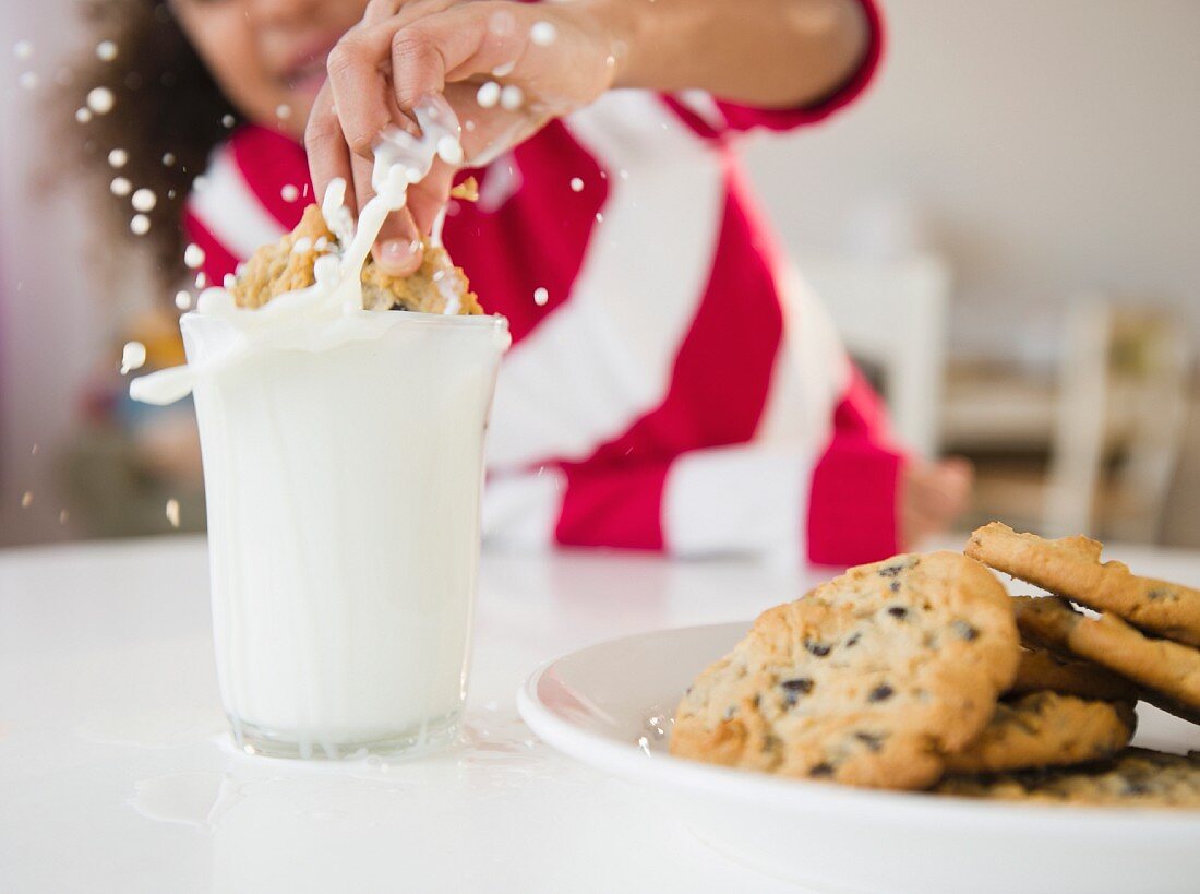 Mixed race girl dunking cookie into milk