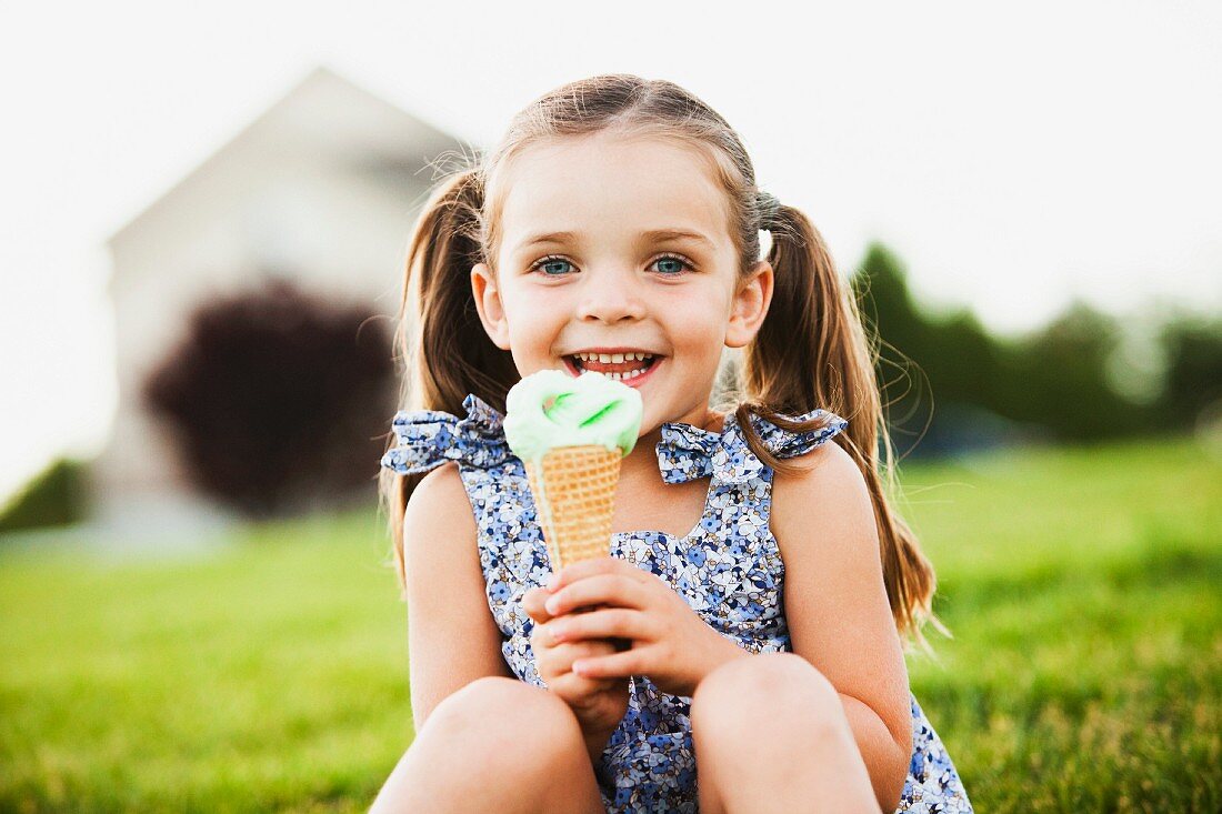 A girl sitting in a meadow holding an ice cream cone