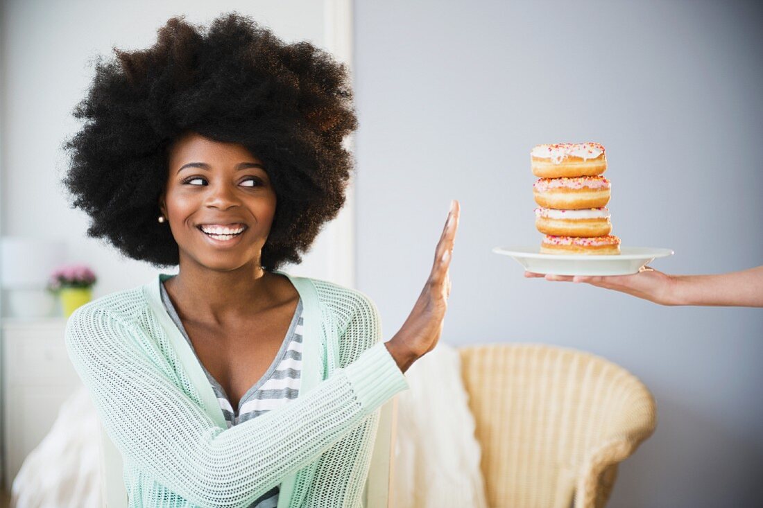 An African-American woman declining a stack of doughnuts