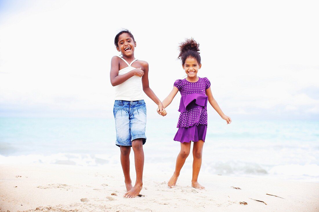 Two dark-skinned girls standing on beach hand in hand