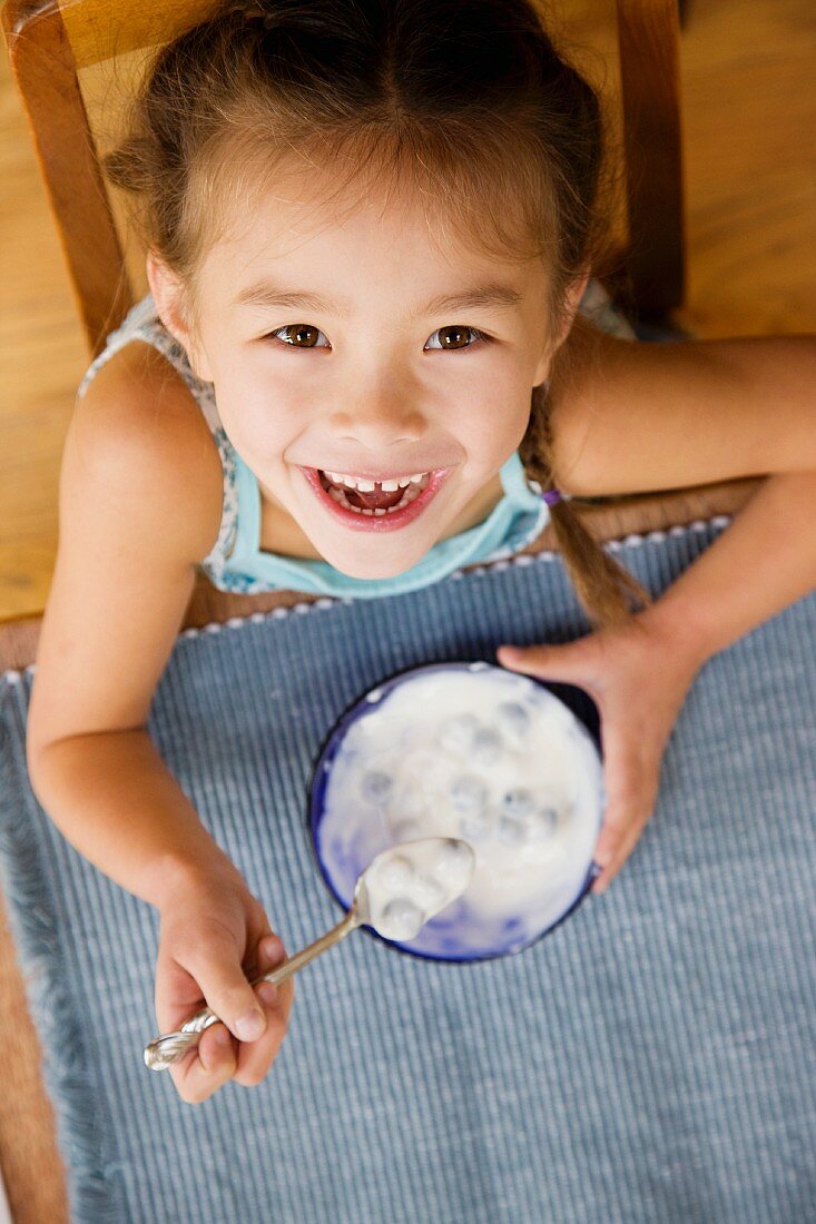Mixed race young girl eating yogurt with spoon