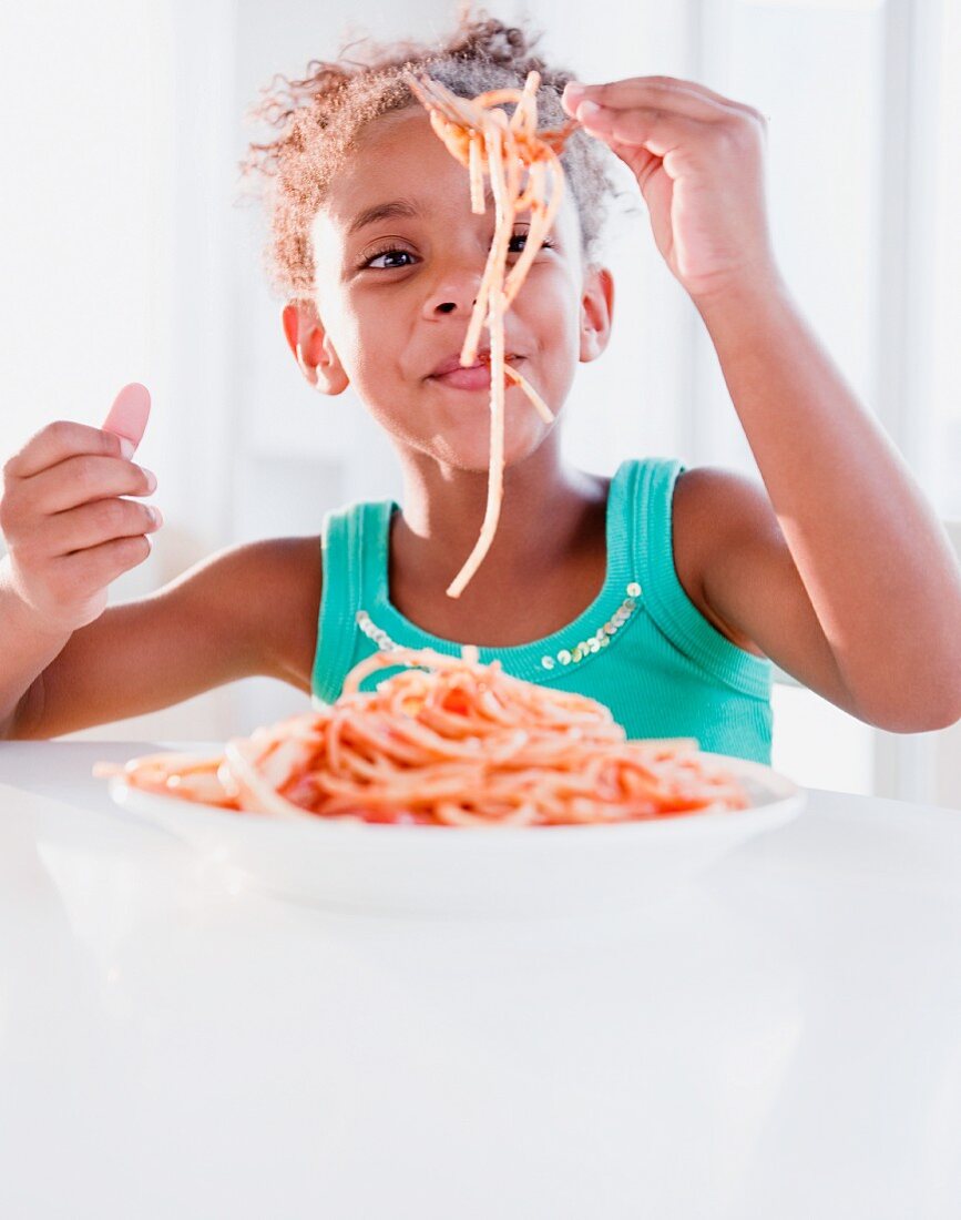 Mixed race girl eating spaghetti