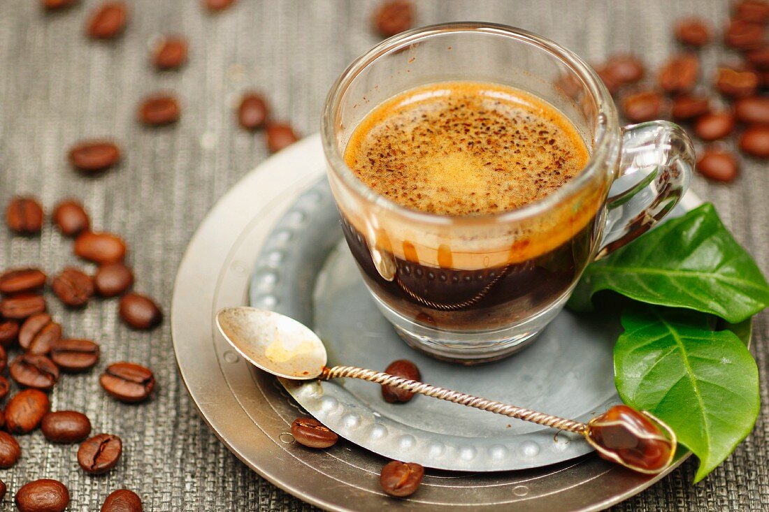 Espresso im Glas mit Kaffeeblatt und Kaffeebohnen