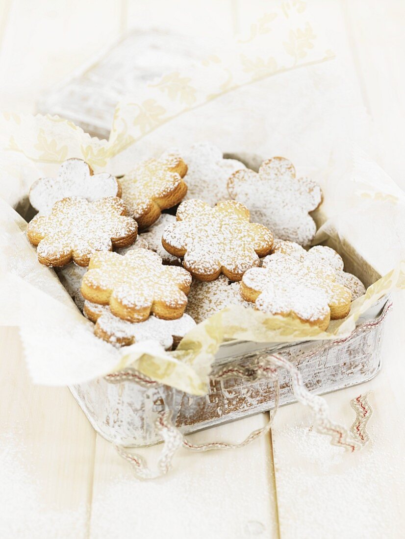 Flower-shaped biscuits with icing sugar in a biscuit tin
