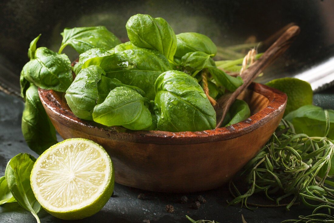 wooden bowl of fresh basil and half of lime over dark bakground