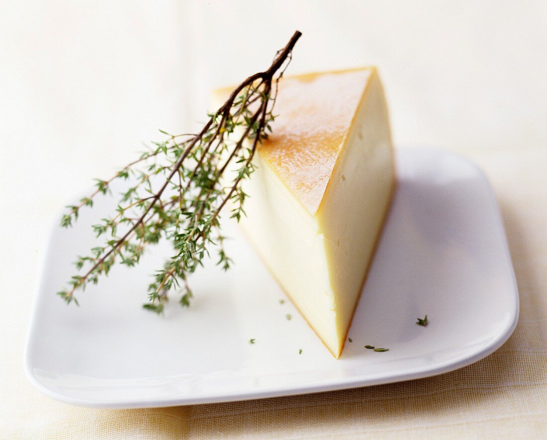 A wedge of Raclette cheese with a sprig of fresh thyme on a plate