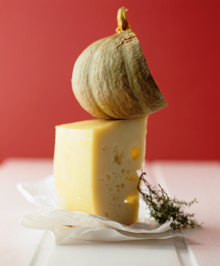 A still life featuring Mondseer cheese, squash and a sprig of thyme