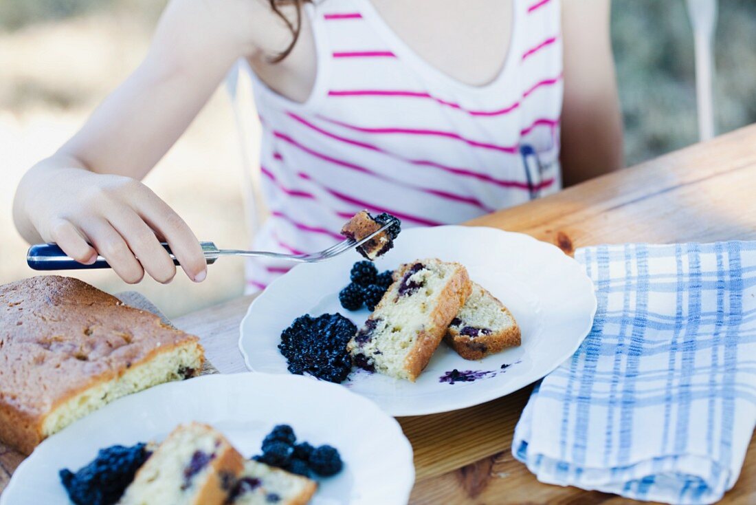 Mädchen isst Brombeerkuchen im Garten