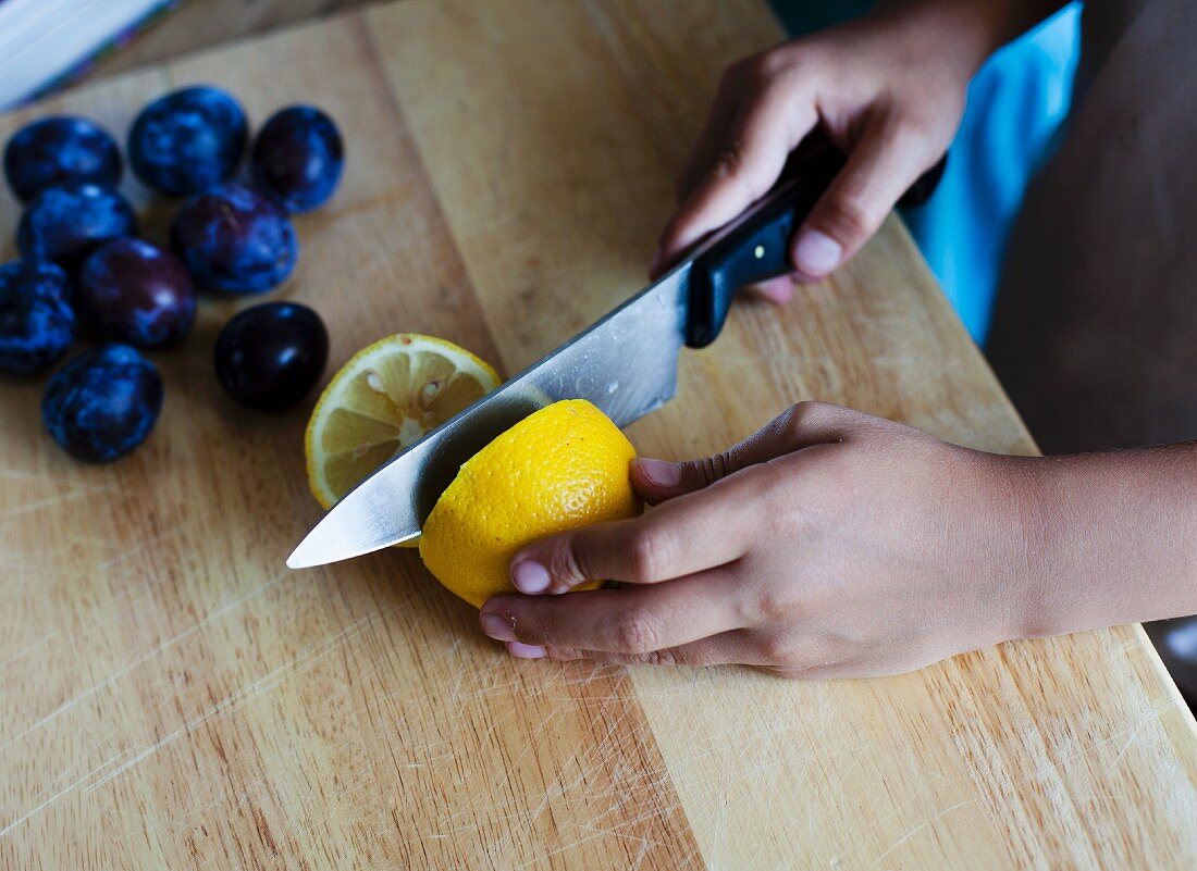 A girl cutting a lemon in half with a knife