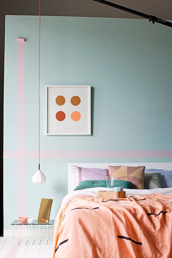 Blanket and cushions on bed against pastel turquoise wall with washi tape stripes and minimalist pendant lamp