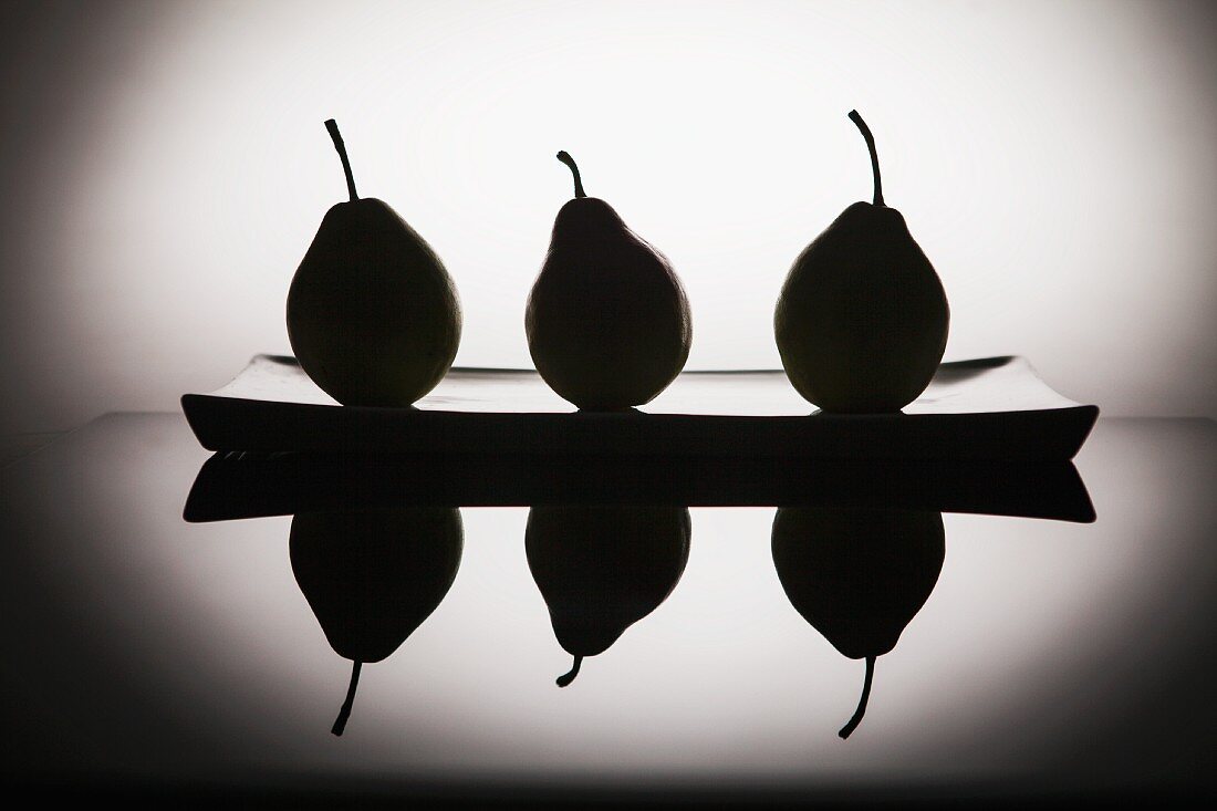 Black silhouettes of pears on a plate, and reflection