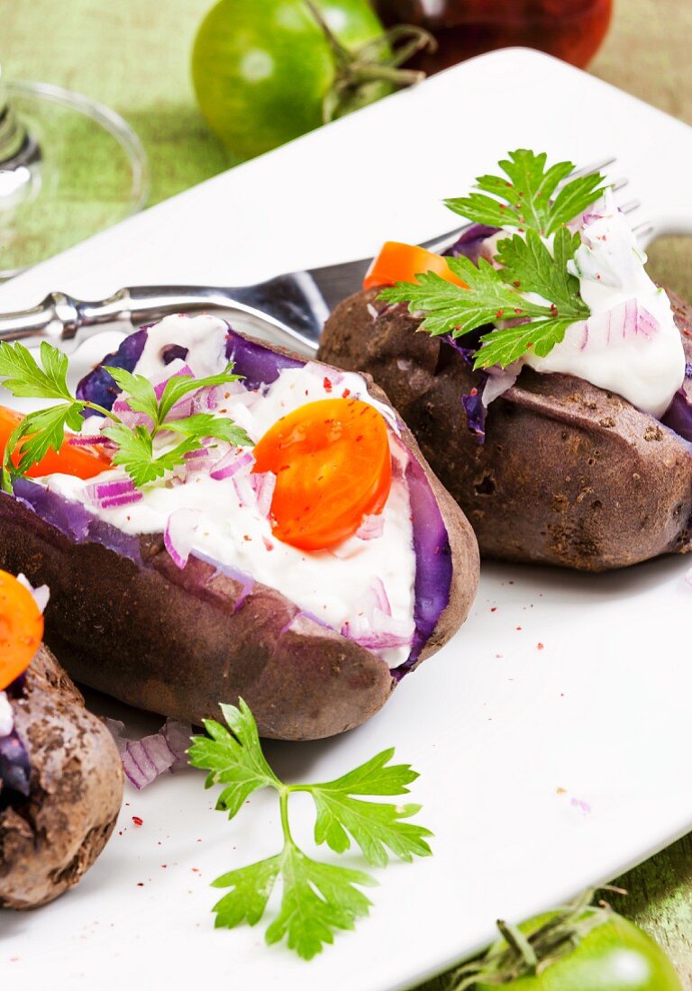 Purple baked potatoes with sour cream, onions and tomatoes