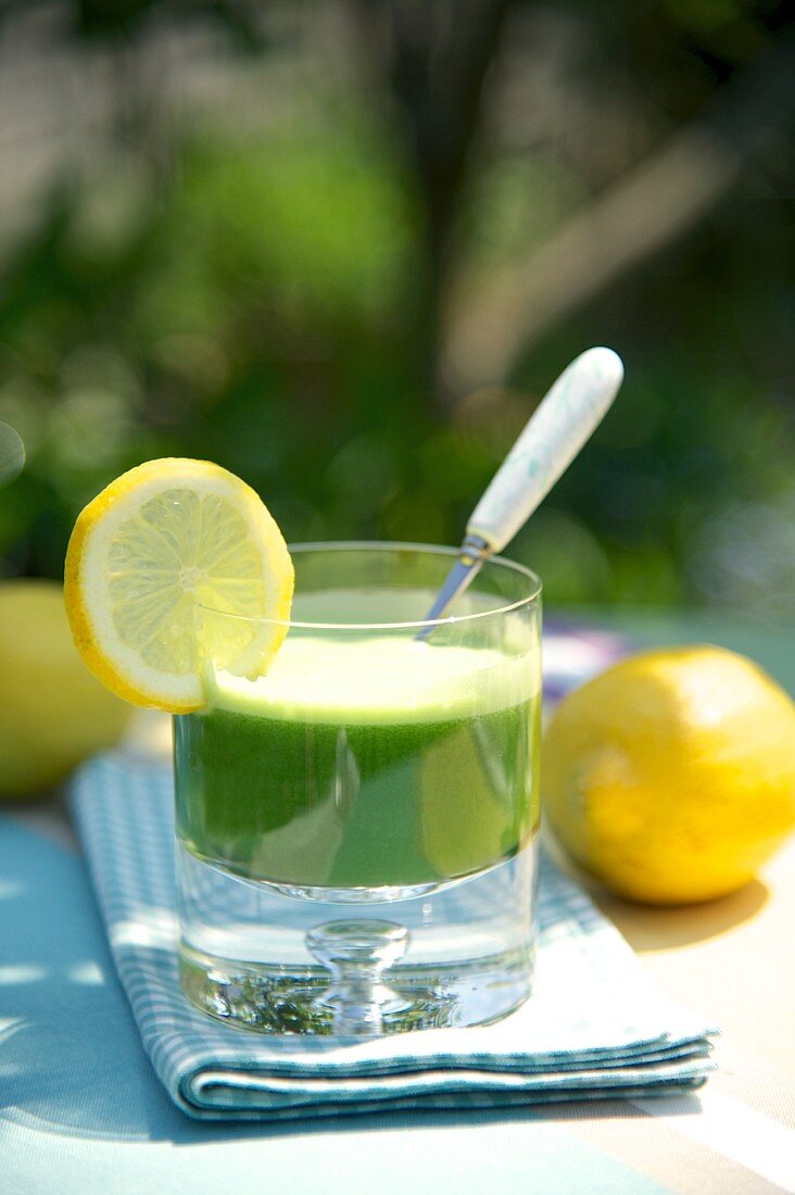 Spinat-Zitronen-Drink mit Zitronenscheiben auf Gartentisch