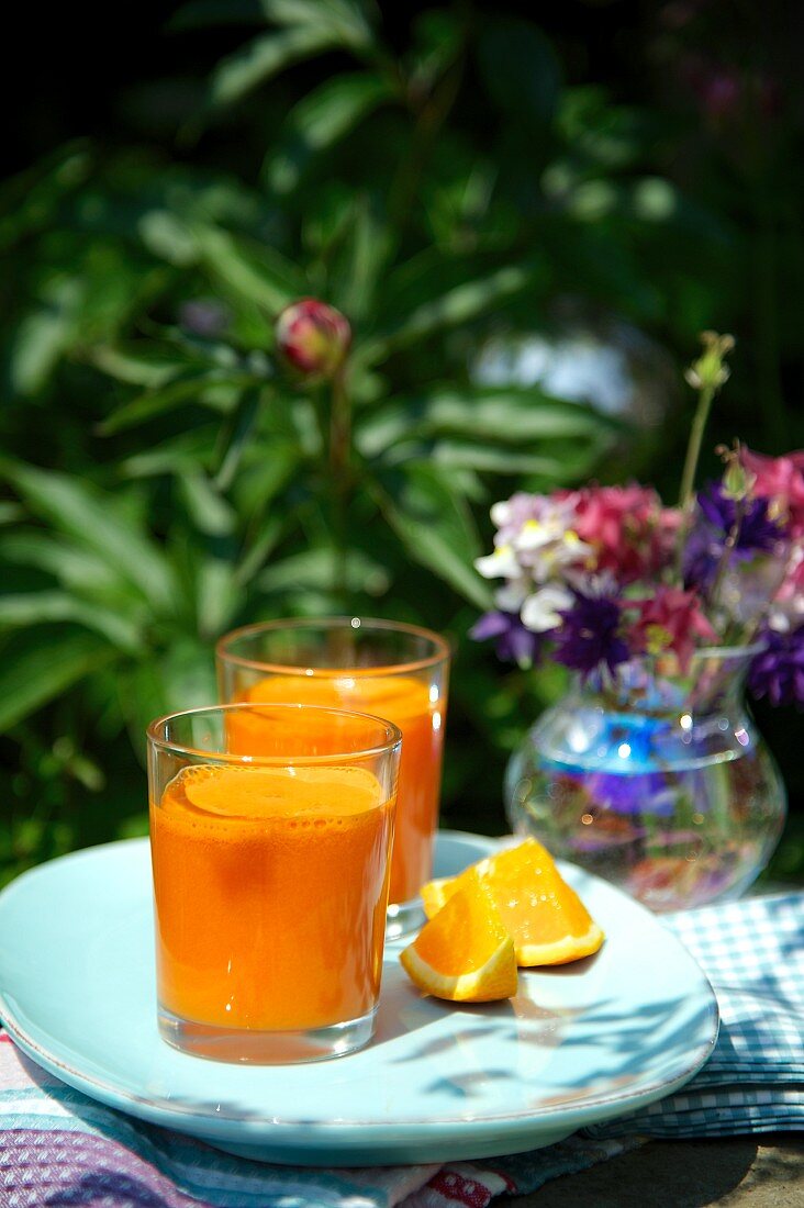 Zwei Orangen-Möhren-Drinks auf Gartentisch