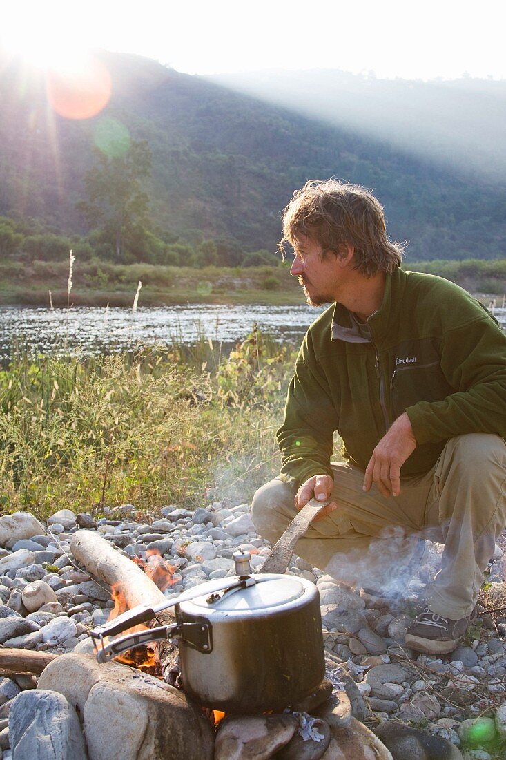 Man Cooking Over a Camp Fire at Sunrise