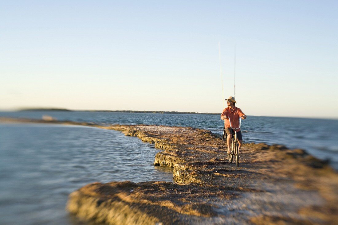 Man Riding Bicycle With Fishing Rods on Rocky Jetty, Florida Keys, USA