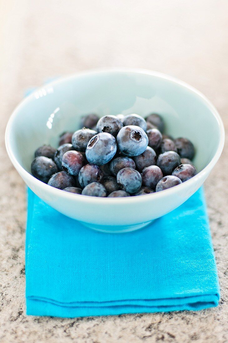 Blaubeeren in einer weissen Schale auf azurblauer Serviette