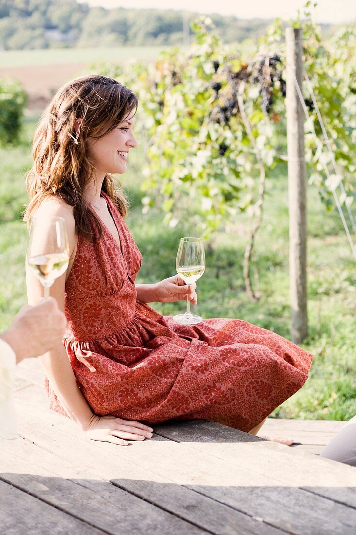 Frau mit einem Glas Weißwein auf Holzterrasse im Weinberg