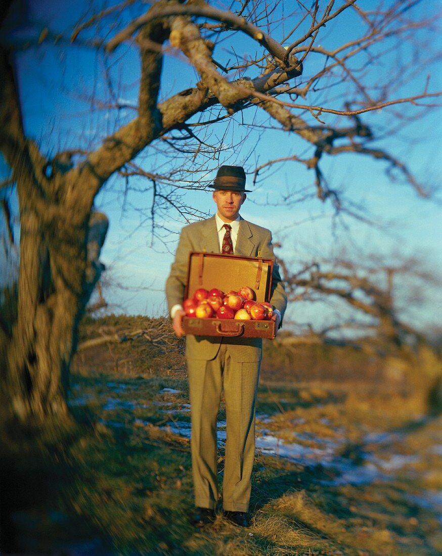 Mann hält einen Koffer mit Äpfeln